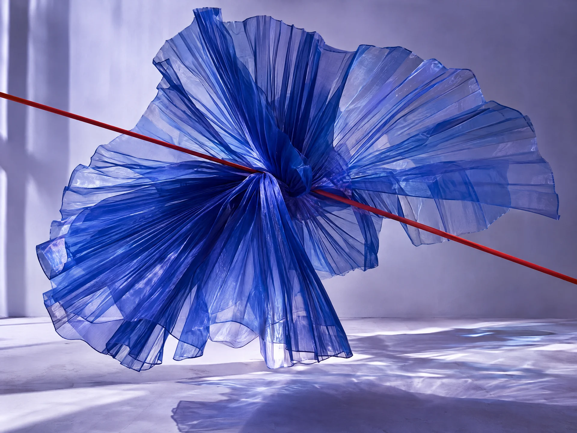 A translucent ultramarine sculpture with a fine red axis, suspended in a lavender space.